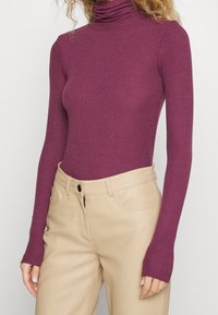 Bordeauxkleurige coltrui van ribgebreide stof met lange mouwen, gecombineerd met beige high-waisted broek met voorzakken en een rits.