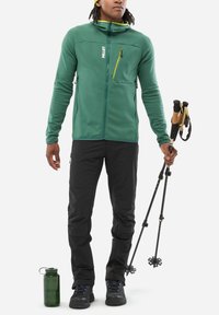 Green fleece jacket with zippered chest pocket, black hiking pants, black hiking shoes, and trekking poles. Includes green water bottle.