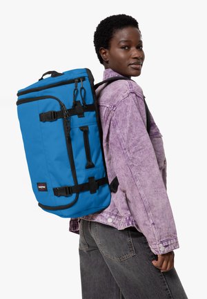 Blauer Rucksack mit schwarzen Akzenten, mehreren Riemen und Reißverschlüssen, in rechteckiger Form und aus strapazierfähigem Material. Logo an der Seite sichtbar.