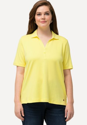 Kortærmet gul polo-shirt med krave, der har en tre-knaps lukning og en afslappet pasform, parret med mørkeblå jeans.