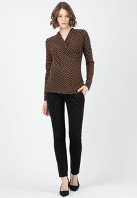 Braun und schwarz gestreiftes Langarmshirt mit Wickeldesign, kombiniert mit schlanken schwarzen Hosen und schwarzen spitz zulaufenden High Heels.