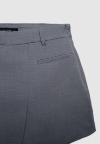 Graue Shorts aus leichtem Stoff, mit flacher Front, seitlichen Taschen und Reißverschluss, sauberen Nähten und minimalen Details.