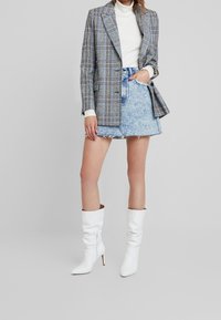 Blazer a quadri grigio, dolcevita a coste bianco, minigonna in denim consumato e stivali bianchi al ginocchio con tacchi a spillo.