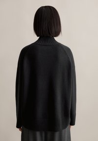 Μαύρος πουλόβερ με γιακά, κατασκευασμένος από μαλακό ύφασμα, με ριγωτό λαιμό και τελειώματα, και χαλαρή γραμμή με κατεβασμένους ώμους.