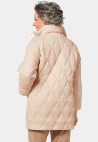 Gestepptes Kleidungsstück in soft-beige mit einem diamantge quilteten Muster, hohem Kragen und langen Ärmeln, mit lockerer Passform und strukturiertem Stoff.