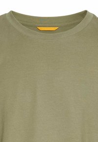 Olivenfarvet bomulds t-shirt med ribbet rund hals. Har en flad søm og et lille orange mærke indeni halsen.