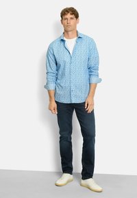Helles blaues Hemd mit kleinem Blumenmuster, hochgekrempelten Ärmeln, kombiniert mit dunklen Jeans und weißen Turnschuhen.