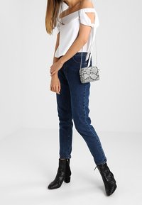 Biały top na ramiączkach z wiązaniami, ciemnoniebieskie dopasowane dżinsy, czarne botki z wężowym nadrukiem sięgające kostki oraz mała torebka z wężowym nadrukiem.