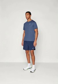 T-shirt et short Nike bleu marine en tissu léger, associés à des baskets blanches avec des accents verts. Design simple et sportif.