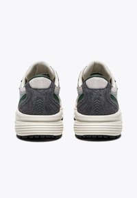 Des baskets avec un talon en daim gris, une tige en mesh blanc, des accents verts et une semelle texturée avec des rainures prononcées pour l'adhérence.