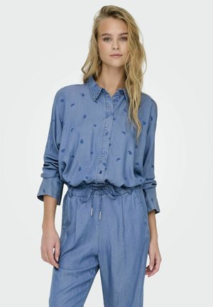 Camicia di denim con chiusura a bottoni, di colore azzurro chiaro e con delicate ricami floreali. Presenta un colletto e maniche lunghe, con una vestibilità comoda.