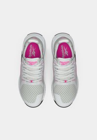 Balti un roz Reebok skriešanas apavi ar acu putām un auklām, redzami no augšas uz balta fona.