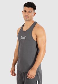 Grijze geribbelde tanktop met witte tekst, voorzien van brede armsgaten en een ronde halslijn, gecombineerd met bijpassende shorts. Zachte stofstructuur.