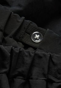 Tessuto nero con una texture arricciata e un dettaglio di bottone trasparente. Il bottone ha un design decorativo e fissa un elastico in vita.