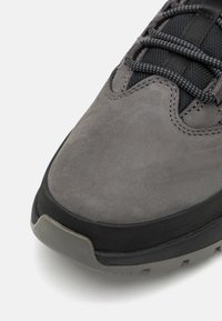 Gray suede shoe with a rubber outsole, textured mesh details, and contrasting black laces. Rounded toe and reinforced edges visible.