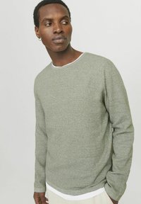 Pull long à manches longues texturé vert avec un col rond et une bordure blanche. Le tissu présente un motif tissé subtil, offrant une apparence confortable.
