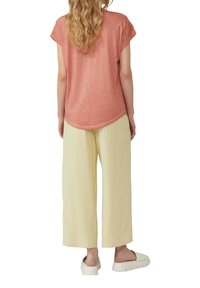 Korte mouwen, koraalroze shirt met een ronde zoom, gecombineerd met losse, lichtgele wijde broek en crèmekleurige instappers.