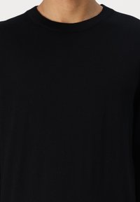 Camisa negra de manga larga hecha de tela suave, con un escote redondo y una textura lisa. Sin patrones visibles ni elementos metálicos.
