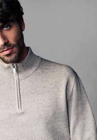 Lys grå, struktureret quarter-zip sweater med høj krave og strikkemønster, der har en elegant sølv lynlås.