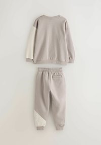 Gray sweatsuit with a crew neck top and elastic waistband pants. Top features white sleeves; pants have a diagonal white panel with embossed text.