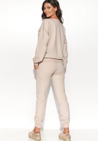 Beżowy zestaw odzieży dresowej składający się z luźnej bluzy i zwężających się spodni dresowych, wykonany z miękkiego materiału. Zauważalne detale to mankiety na rękawach i nogawkach.