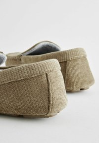 Baskets beiges à enfiler avec un tissu texturé, un col rembourré et une doublure intérieure douce. La pointe arrondie et la semelle en caoutchouc flexible améliorent le confort.
