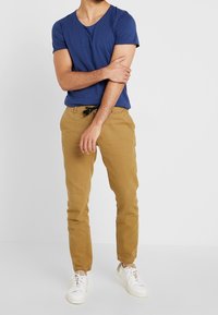 Mörkblå t-shirt med kort ärm och djup v-ringning, kombinerad med khaki chinos med svart dragsko. Vita sneakers fullända outfiten.