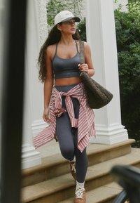 Reggiseno sportivo grigio e leggings abbinati a una maglietta a righe rosse e bianche annodata in vita. Borsa marrone trapuntata e scarpe da ginnastica neutre.