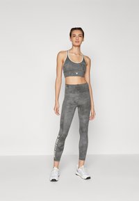 Sports bra and leggings set in gray with light accents. Textured fabric, form-fitting design, and logo detail on leggings.