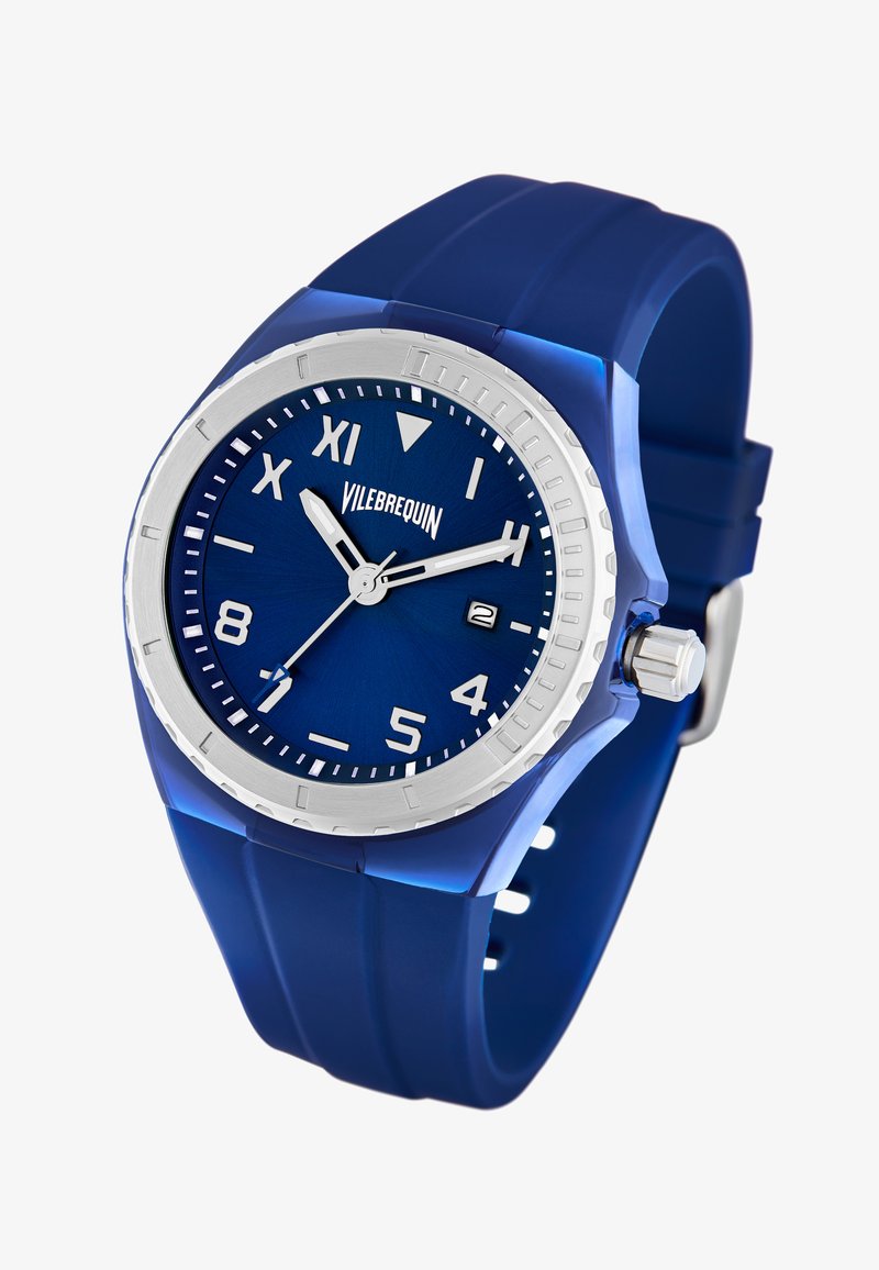 Blå silikon klocka med silverfärgad bezel, blå urtavla med vita timmarkörer och visare, datumvisning och en strukturerad rem.