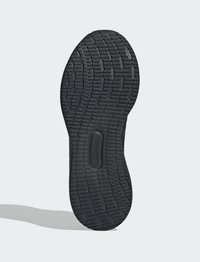 Semelle de chaussure noire avec un motif de bande de roulement texturé, comportant des rainures et des crêtes pour une meilleure adhérence. La forme est arrondie au niveau des orteils et du talon.