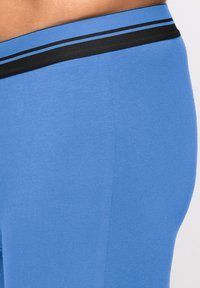 Leggings bleu clair avec une texture douce, dotés d'une taille noire avec une double bande bleue. Vue en gros plan montrant la forme et l'ajustement.