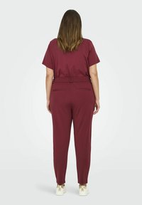 Viininpunaiset väljät housut, joissa on joustava vyötärönauha, sivutaskut ja kapeneva lahjepituus. Yhdistetty kultakoristeisiin tennareihin.