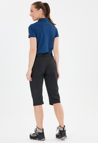 Blå polo shirt, sorte knælange bukser og grå vandrestøvler. Glat stof, skræddersyet pasform, med en let glans på skjorten.