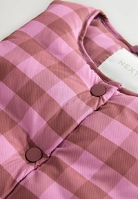 Gilet matelassé rose et marron à carreaux avec un col rond et deux boutons ronds marron à l'avant, fabriqué en tissu synthétique brillant.