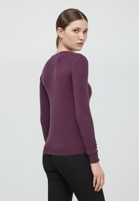 Maglione viola a maniche lunghe con collo rotondo, design aderente e polsi a coste. Il materiale sembra morbido e testurizzato.