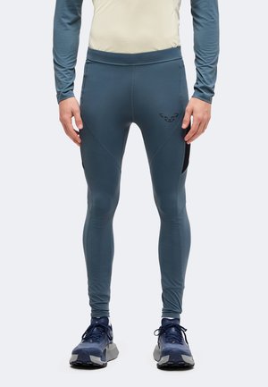 Homme portant des leggings de sport bleus et des chaussures de course bleu marine, debout les mains détendues le long du corps.