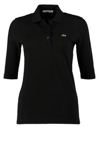 Polo noir pour femme avec manches trois-quarts, patte de boutonnage à deux boutons, et petit logo crocodile vert de Lacoste sur la poitrine.
