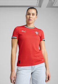 Rde majica s kratkimi rokavi in okroglim ovratnikom, z belim in zelenim robom. Vključuje logotip Puma in grb portugalske reprezentance.