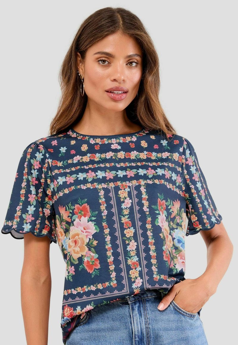 Blouse à manches courtes à motifs floraux sur une base bleu marine, avec des motifs floraux intriqués, des bords de manches festonnés et une coupe décontractée.