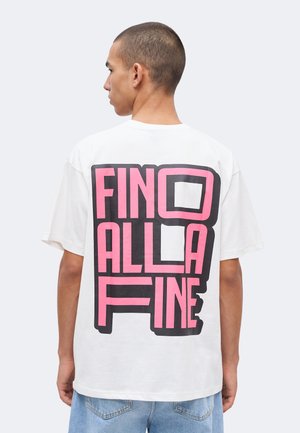 Nuori mies, jolla on lyhyet hiukset, nähty takaa, pitää valkoista T-paitaa, jossa on suuri vaaleanpunainen ja musta lohkokirjoitus selässä.