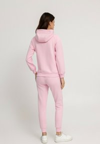 Sweat-shirt rose avec capuche et pantalon ajusté assorti. Fabriqué en un matériau doux, avec des poignets côtelés et une coupe décontractée. Baskets blanches.