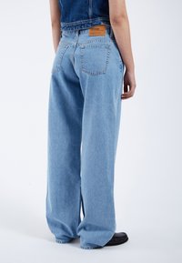 Jeans de mezclilla de pierna ancha en azul claro, con un diseño clásico de cinco bolsillos y un parche trasero de cuero marrón.