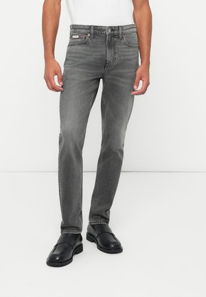 Schmal geschnittene graue Denim-Jeans mit einem ausgewaschenen Finish, klassische Five-Pocket-Design und Metallbeschläge. Getragen mit schwarzen Schuhen.