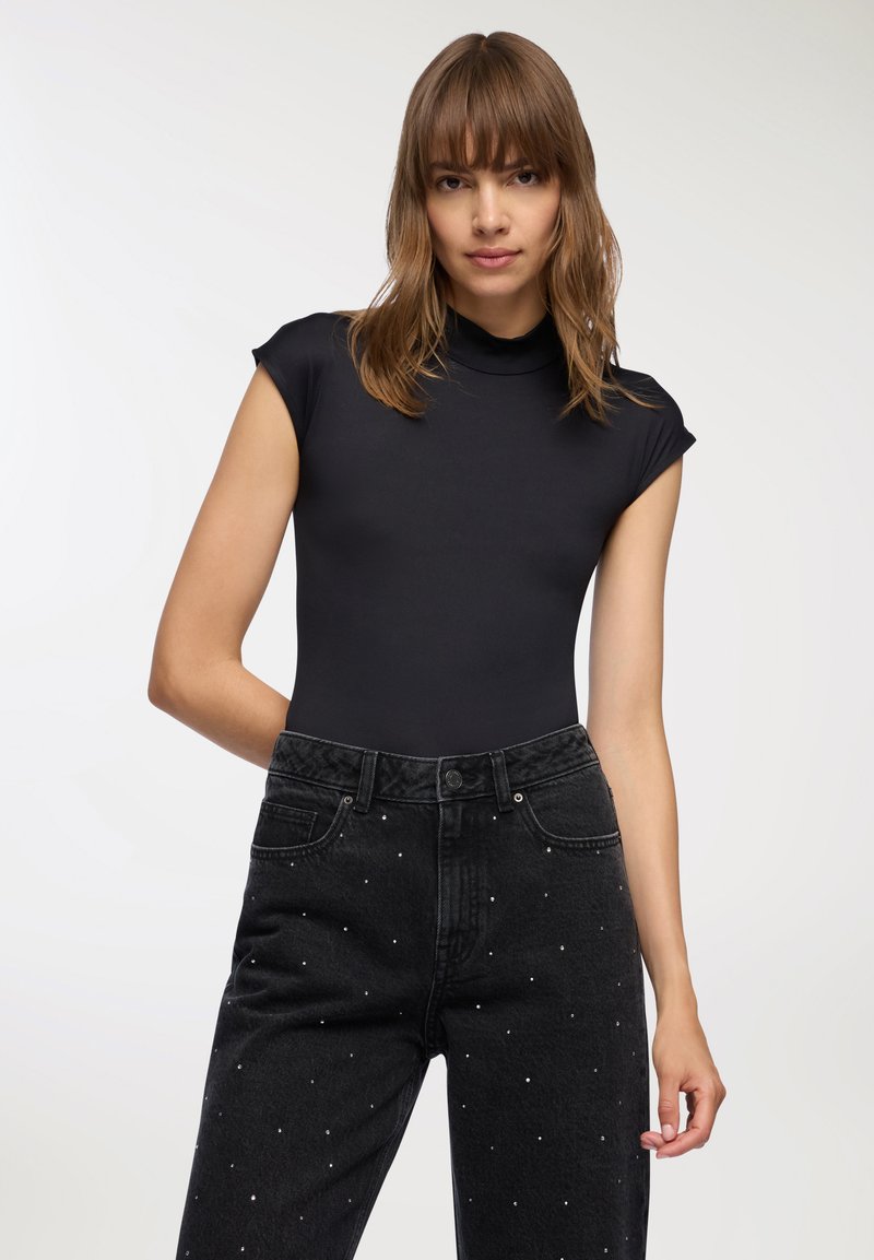 Czarny dopasowany bodysuit z wysokim dekoltem, połączony z czarnymi dżinsami z wysokim stanem z metalowymi wstawkami. Gładka struktura materiału.