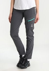 Grijze outdoorbroek met een slanke pasvorm, voorzien van een ritszak in turquoise en een wit logo op de dij. Duurzame stof met een gladde textuur.