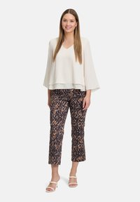Top crema con scollatura a V e maniche lunghe abbinato a pantaloni cropped scuri con un motivo, in tonalità marrone chiaro e blu navy, completato da sandali con tacco bianchi.