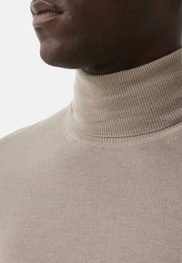 Pull en col roulé beige présentant une texture côtelée. La vue en gros plan met en valeur le tissu lisse, le col haut et les détails de couture.