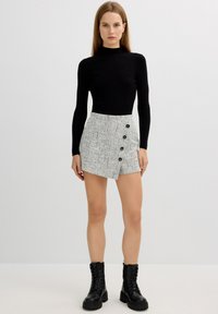 Jersey de cuello alto ribeteado negro combinado con una minifalda de tweed gris que cuenta con cinco botones negros y una abertura lateral, complementado con botas negras con cordones.