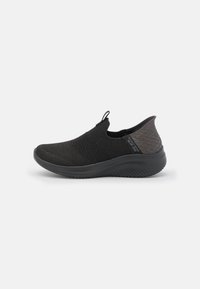 Zapato negro de punto tipo slip-on con parte superior texturizada, abertura elástica y acento en el talón de color contrastante. Suela ligera con surcos para mayor tracción.